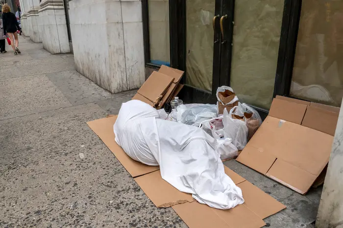 A person wrapped in a white sheet lays on the street on top of a cardboard box